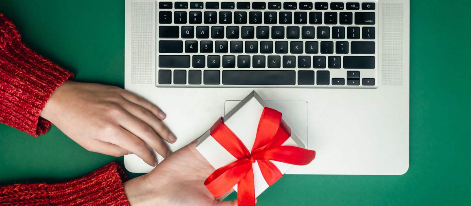 Gift box in female hands on the background of a laptop, the concept of Christmas online shopping, top view.